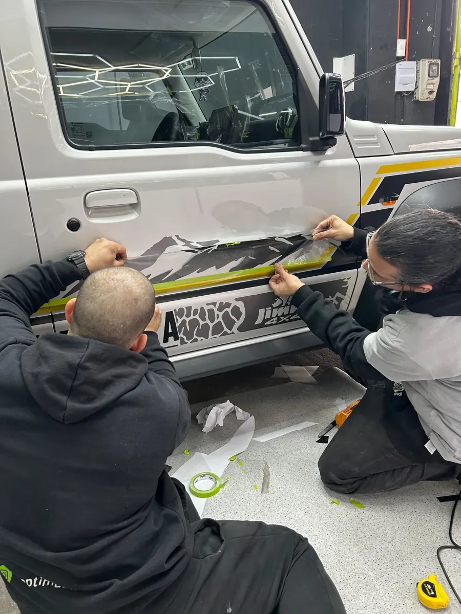 Dos técnicos instalando el vinilo de montañas en la puerta del Suzuki Jimny, Santiago